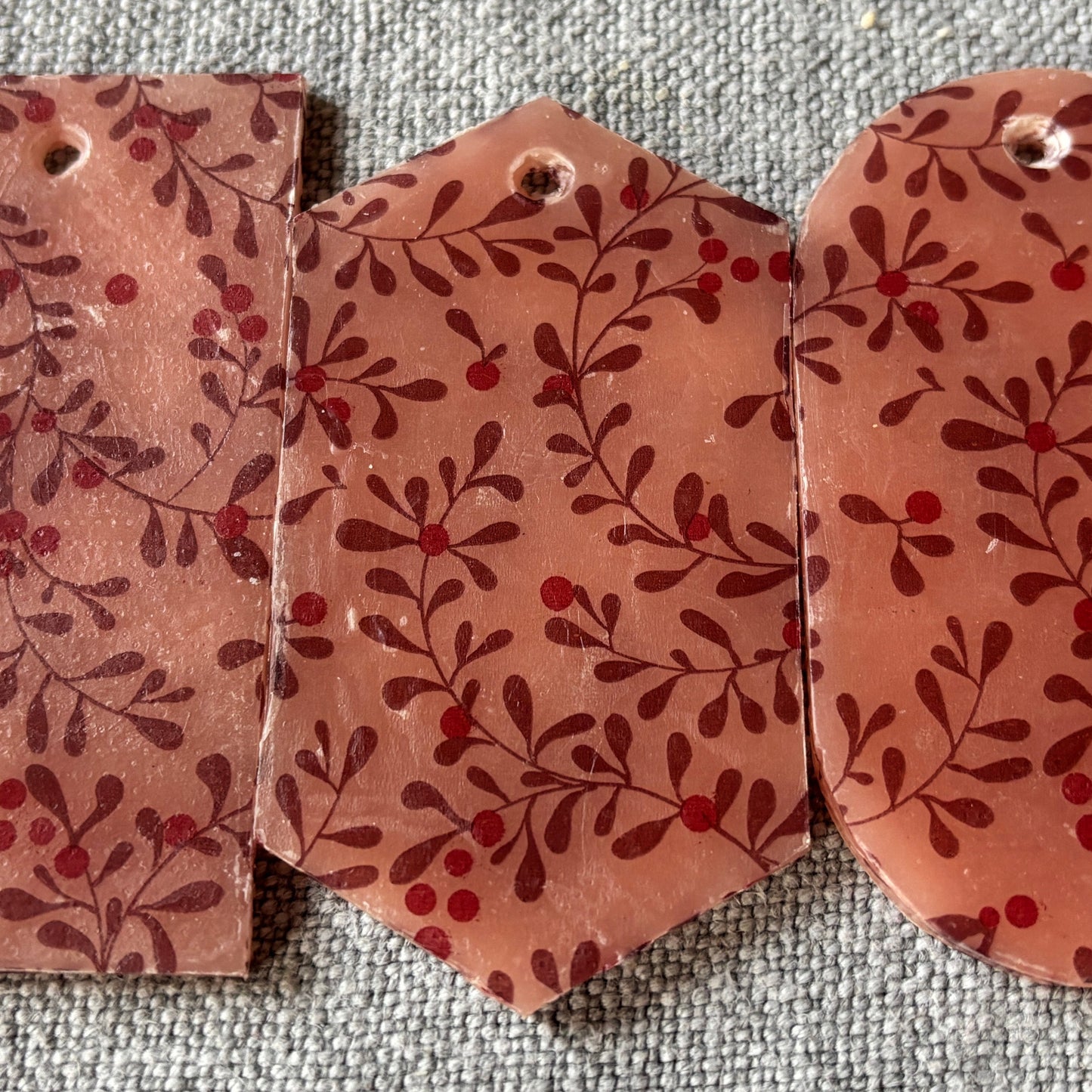 Three pink mistletoe patterned wax decorations on a textured gray surface.
