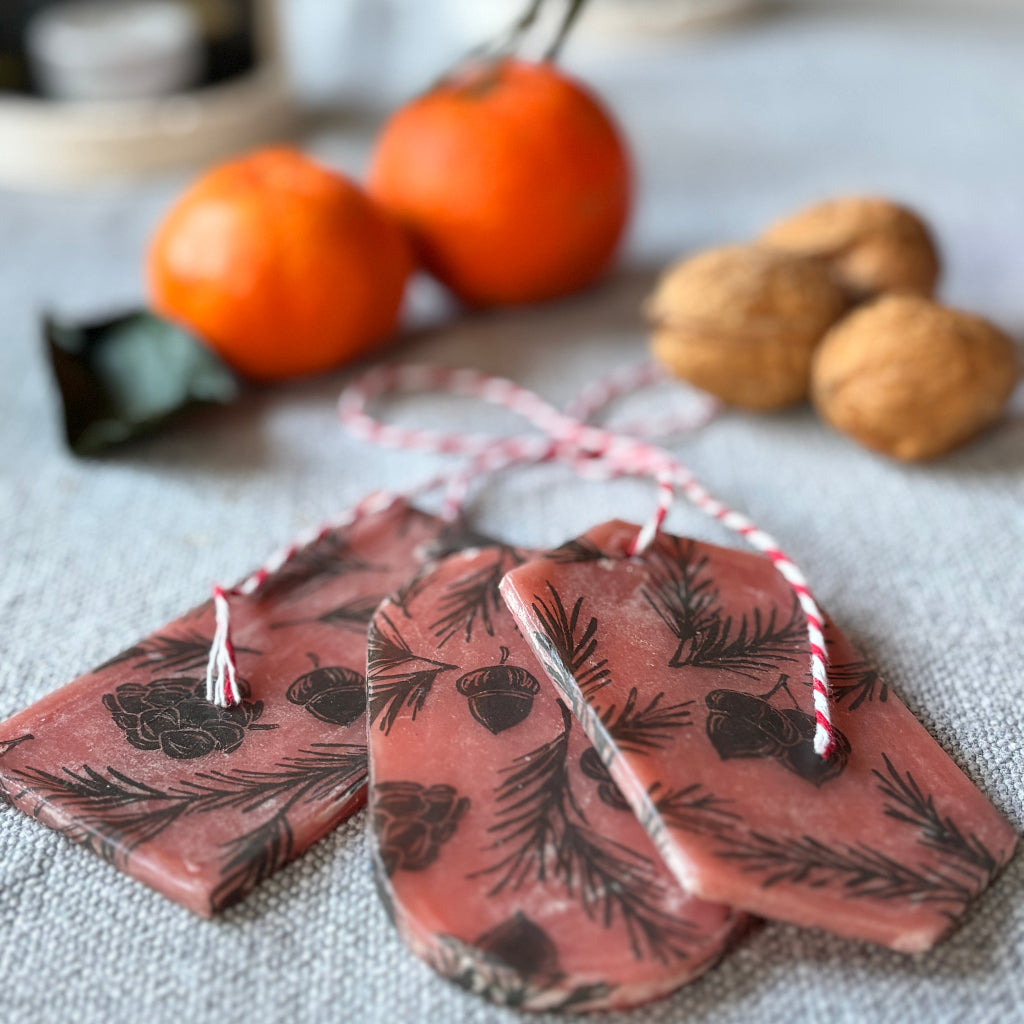 Decorative wax bars with leaf pattern on a textured surface with clementines and nuts in the background.