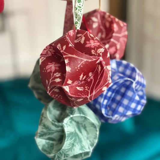 Decorative waxed fabric Christmas baubles decorations in red, blue, and green hanging against a blurred background.