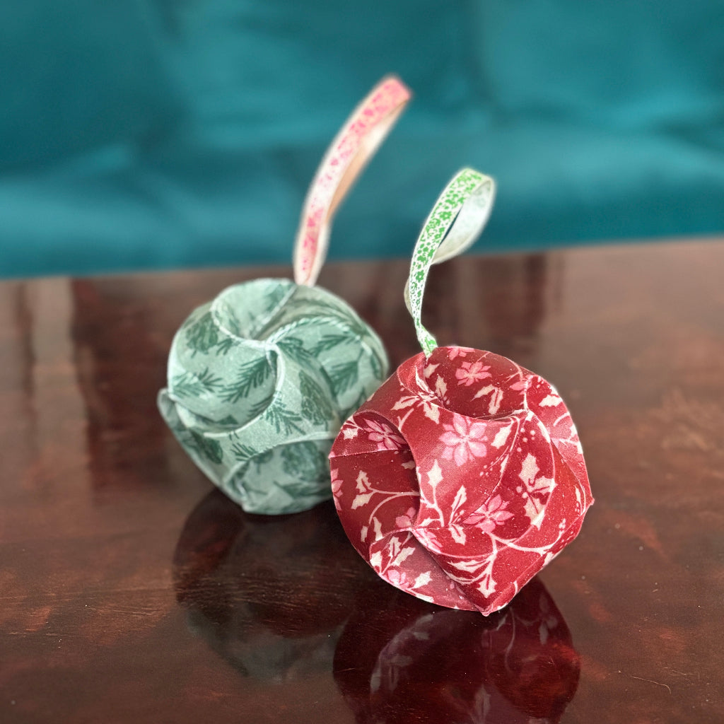 Two waxed fabric christmas baubles on a reflective surface with a teal background.
