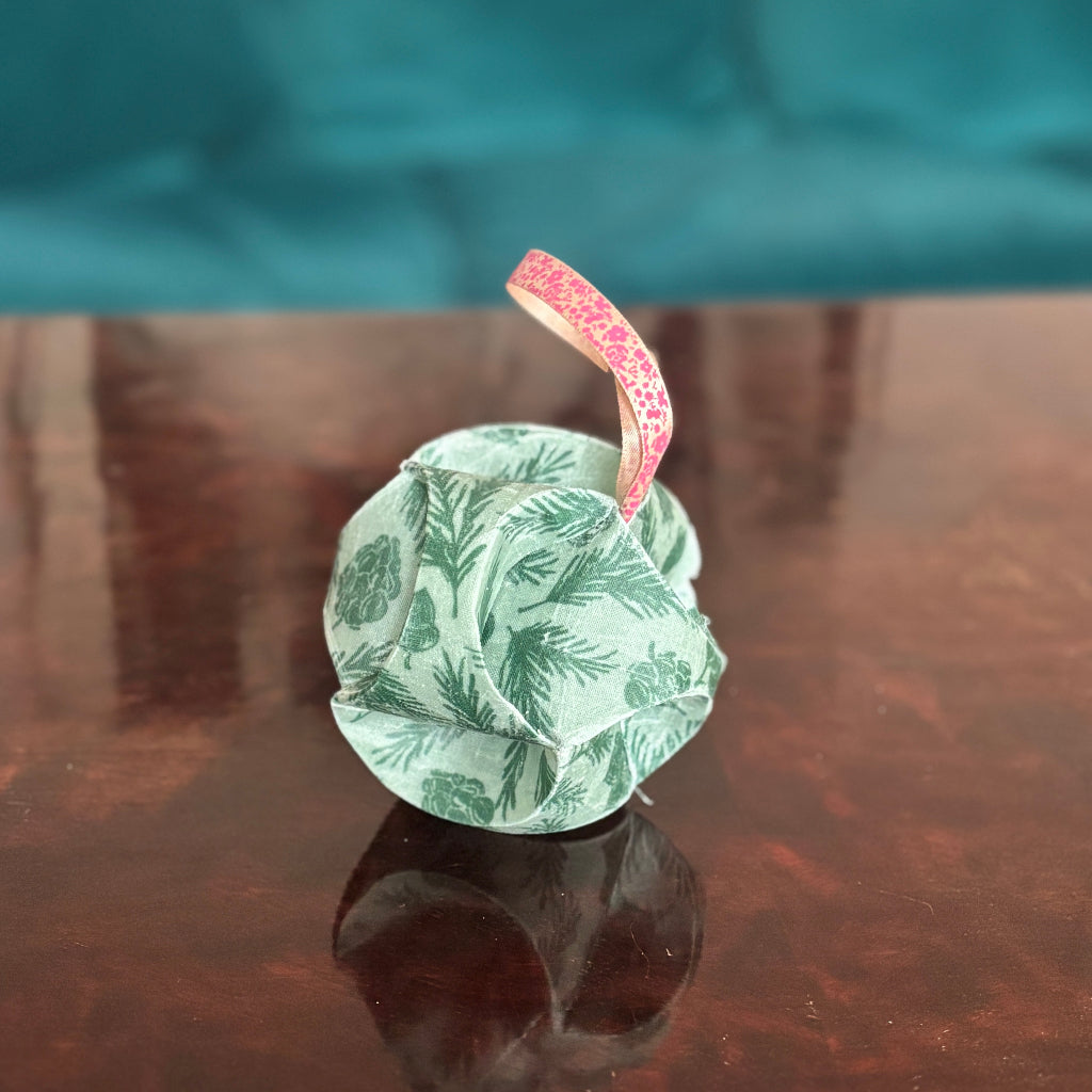 Green floral waxed fabric Christmas bauble ornament with a red string on a reflective surface.