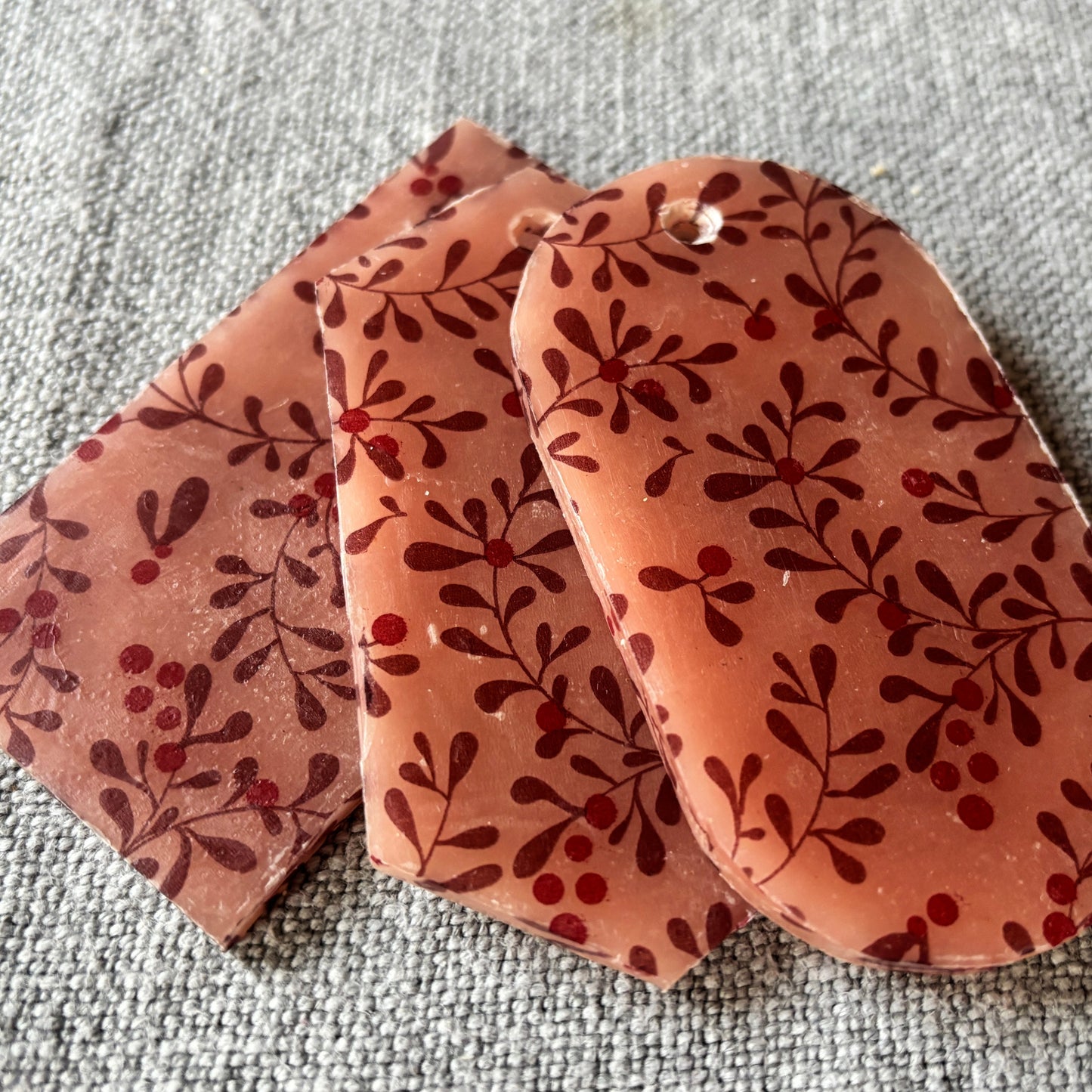 Three pink mistletoe patterned wax decorations on a textured gray surface.